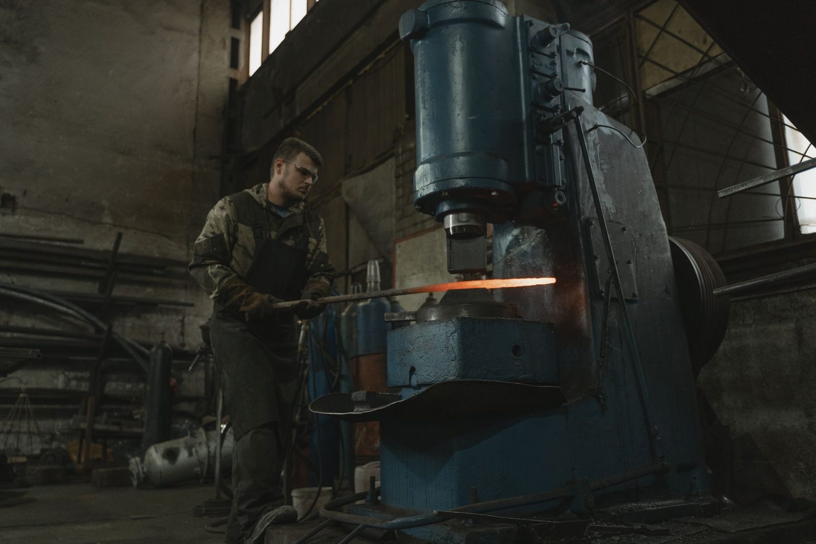 A smith working a glowing bar under a power hammer