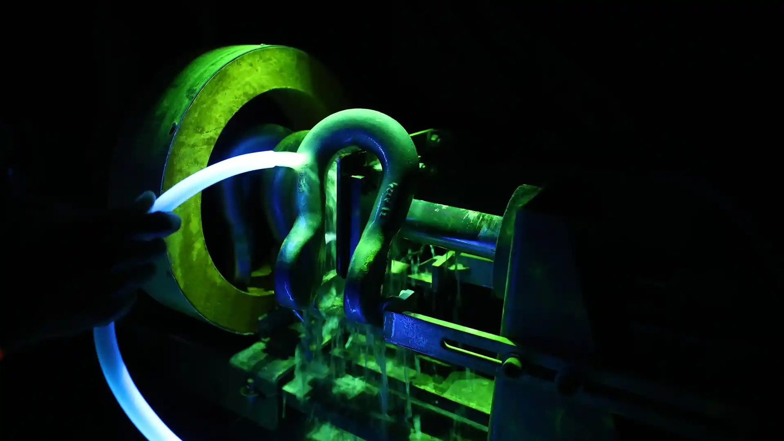 A forged shackle under magnetic particle inspection, glowing under ultraviolet light